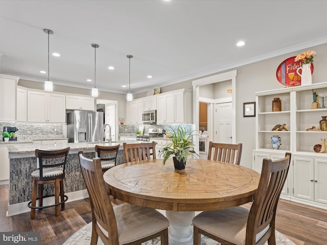 dining space featuring sink, ornamental molding, and dark wood-type flooring