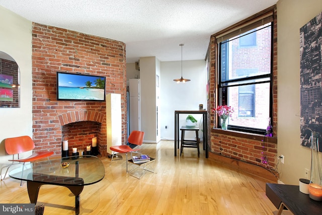 living room featuring hardwood / wood-style floors, a textured ceiling, and a brick fireplace