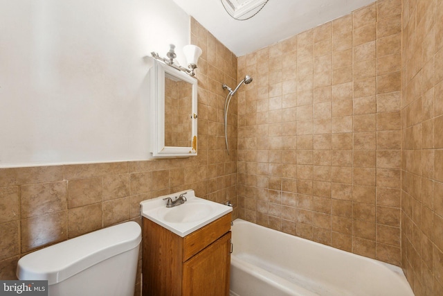 full bathroom featuring vanity, tiled shower / bath combo, toilet, and tile walls