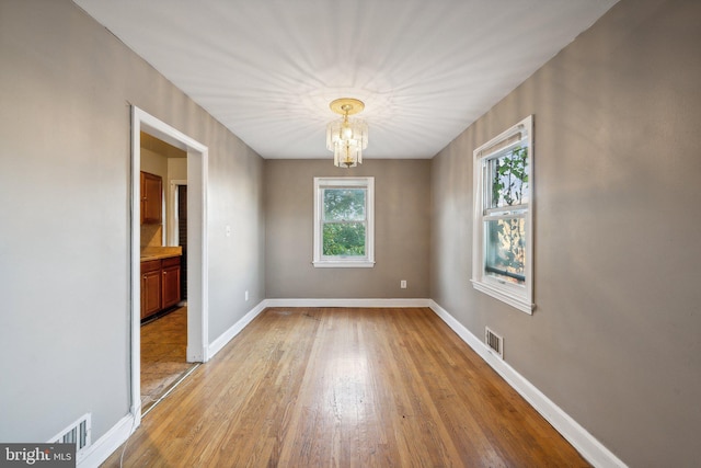 empty room with light hardwood / wood-style floors and a notable chandelier