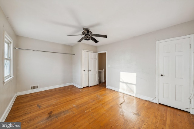 unfurnished bedroom with radiator, multiple closets, wood-type flooring, and ceiling fan