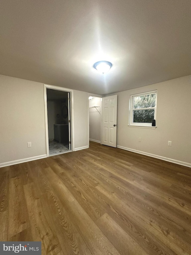 unfurnished bedroom featuring a closet, ensuite bath, a spacious closet, and hardwood / wood-style floors