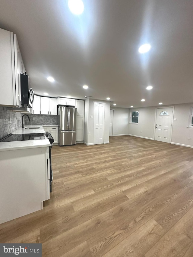 kitchen with light hardwood / wood-style floors, stainless steel refrigerator, decorative backsplash, and white cabinets