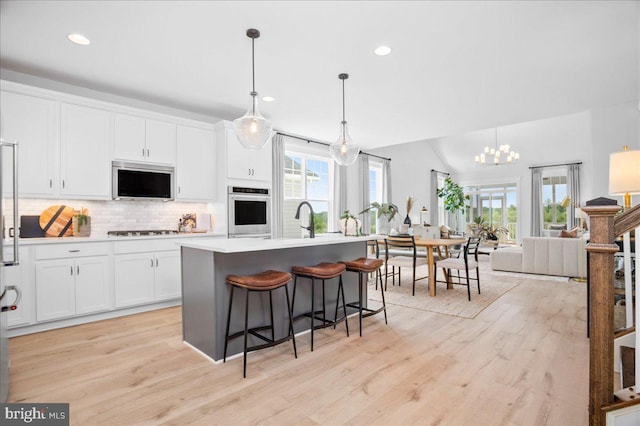 kitchen with appliances with stainless steel finishes, a healthy amount of sunlight, decorative light fixtures, and an island with sink