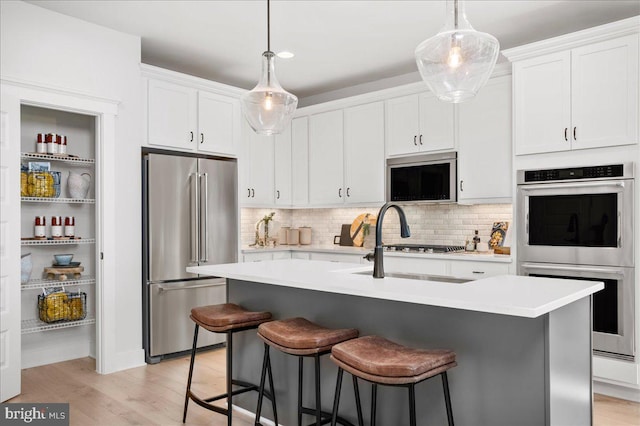 kitchen featuring an island with sink, tasteful backsplash, white cabinetry, light hardwood / wood-style flooring, and appliances with stainless steel finishes