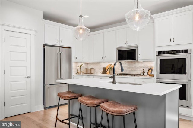 kitchen featuring tasteful backsplash, light hardwood / wood-style flooring, a kitchen island with sink, white cabinetry, and stainless steel appliances