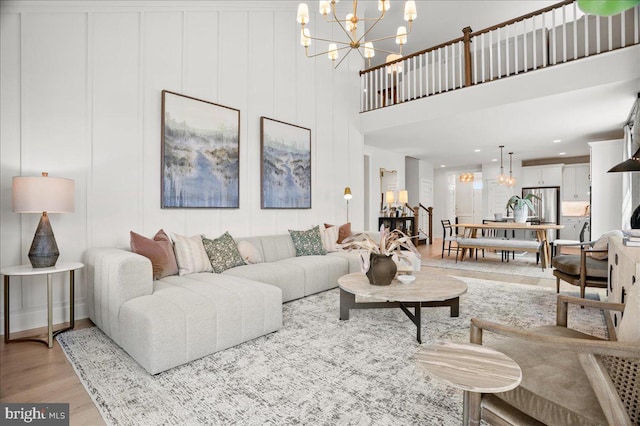 living room with a high ceiling, a chandelier, and light wood-type flooring