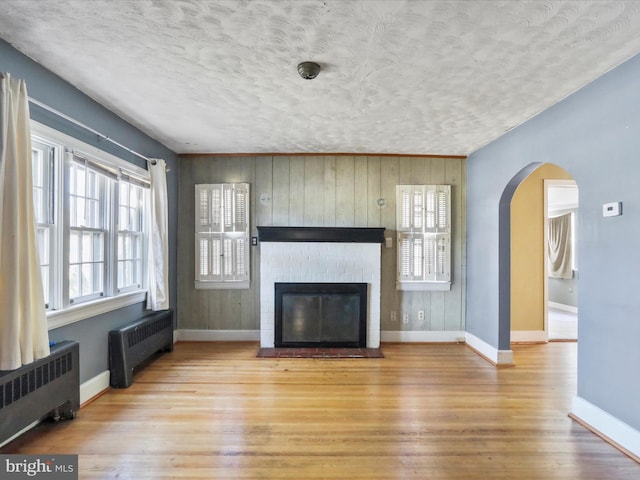 living room featuring light hardwood / wood-style flooring, radiator heating unit, a textured ceiling, and wood walls