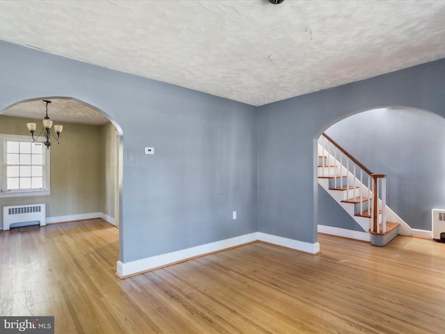 unfurnished living room with radiator, a notable chandelier, a textured ceiling, and light wood-type flooring