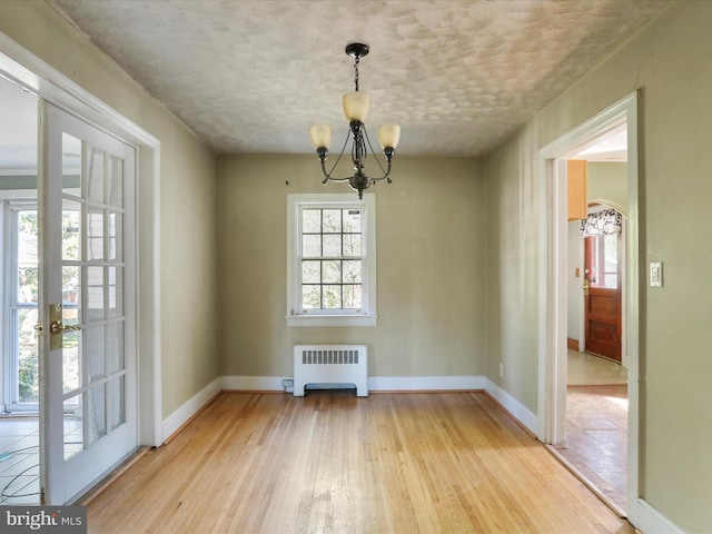 unfurnished dining area with an inviting chandelier, french doors, radiator heating unit, and light hardwood / wood-style floors