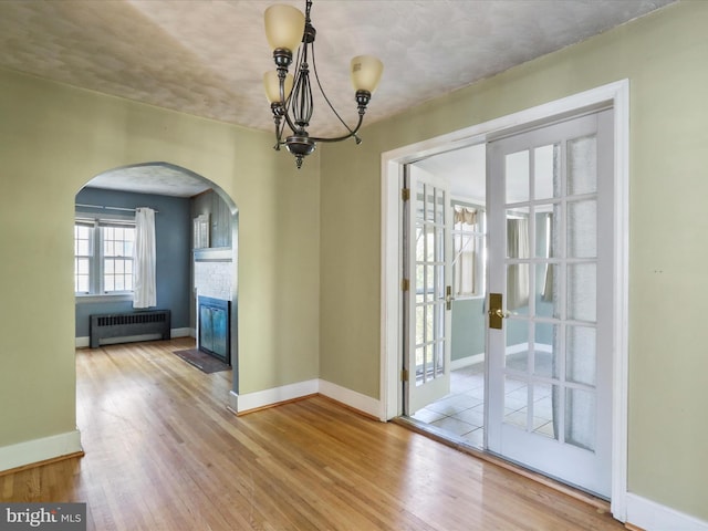 unfurnished dining area featuring light hardwood / wood-style floors, a notable chandelier, radiator heating unit, and french doors