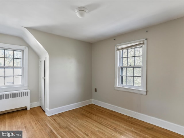 unfurnished room featuring a wealth of natural light, radiator heating unit, and light hardwood / wood-style floors