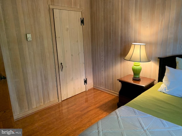 bedroom with light wood-type flooring, wooden walls, and a closet