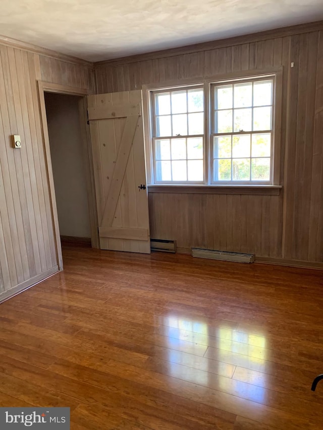 unfurnished room featuring baseboard heating, wooden walls, and wood-type flooring