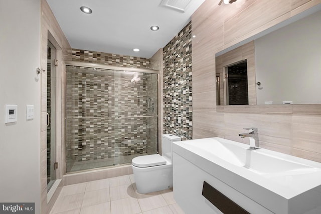 bathroom with vanity, a shower with door, tile walls, tile patterned floors, and toilet