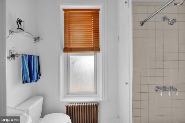 bathroom featuring a tile shower, radiator, and toilet