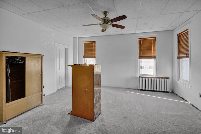 carpeted empty room featuring a paneled ceiling, radiator, and ceiling fan