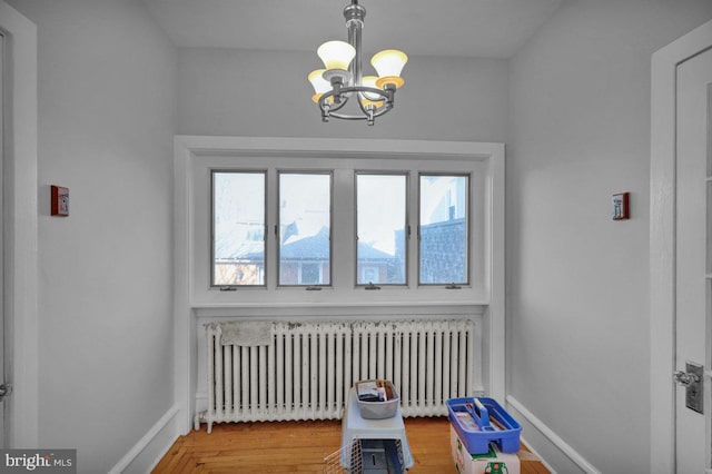 unfurnished room with hardwood / wood-style floors, radiator, and a notable chandelier