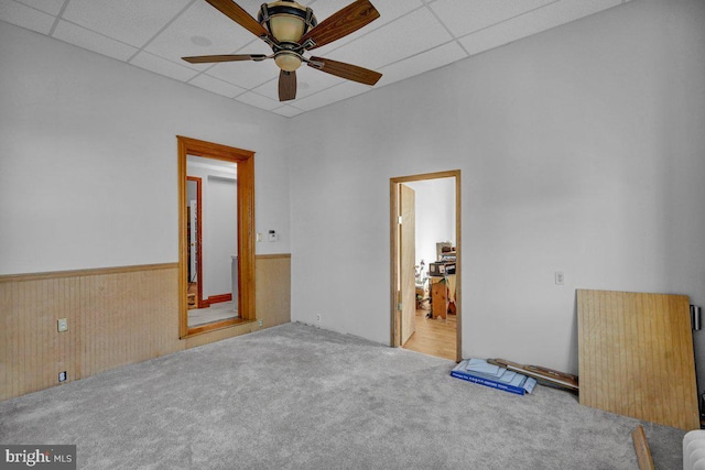 empty room featuring ceiling fan, a drop ceiling, light colored carpet, and wooden walls