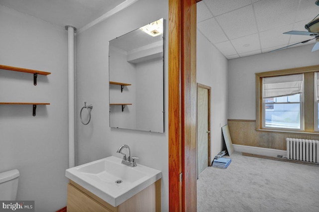 bathroom with a paneled ceiling, vanity, ceiling fan, toilet, and radiator heating unit