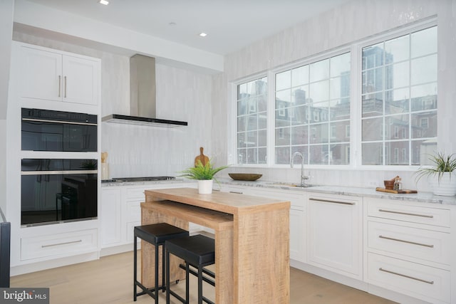 kitchen featuring black double oven, white cabinetry, and wall chimney range hood