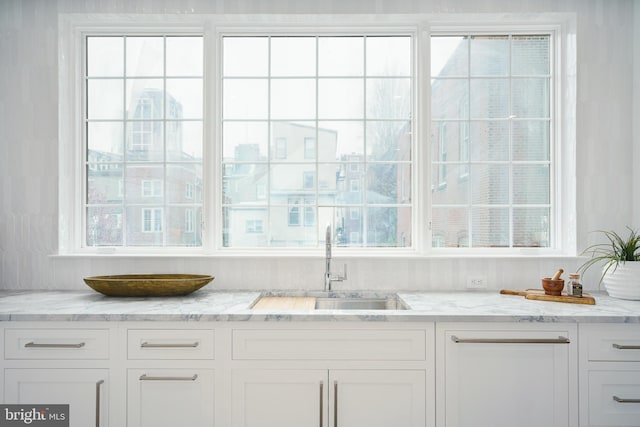 bar featuring white cabinets, sink, and light stone counters