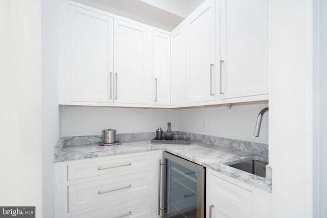 kitchen with white cabinets, wine cooler, light stone counters, and sink