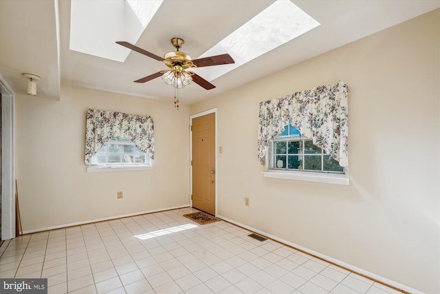 unfurnished room with ceiling fan, a skylight, light tile patterned floors, and a healthy amount of sunlight