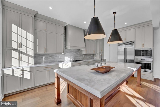 kitchen featuring a sink, decorative backsplash, built in appliances, gray cabinets, and custom range hood