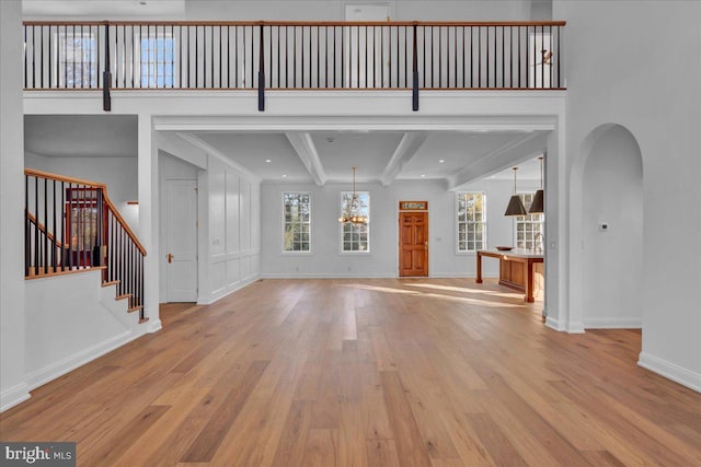 unfurnished living room featuring wood finished floors, arched walkways, beamed ceiling, baseboards, and a chandelier