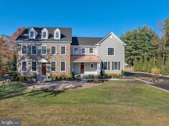 colonial home featuring a front lawn, a standing seam roof, covered porch, stone siding, and metal roof