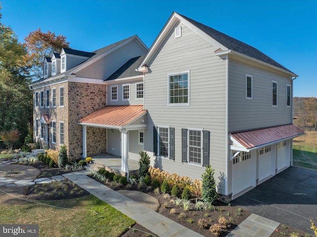 view of front of home featuring metal roof, an attached garage, stone siding, and aphalt driveway