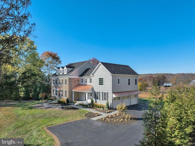 exterior space featuring aphalt driveway, a garage, a standing seam roof, a lawn, and metal roof