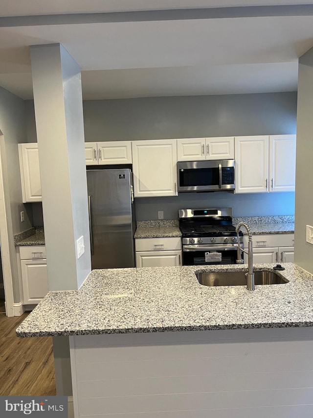 kitchen featuring dark wood-type flooring, sink, white cabinetry, appliances with stainless steel finishes, and light stone counters