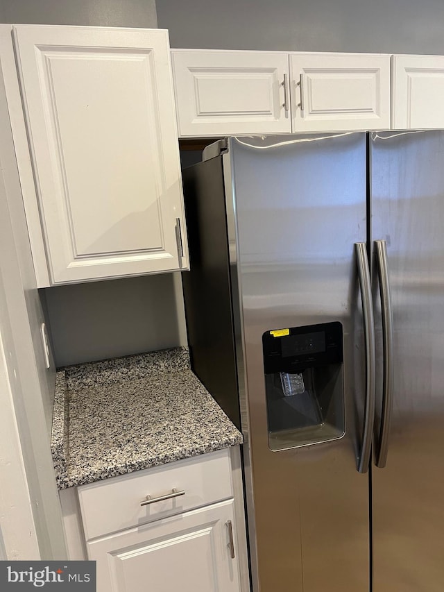 kitchen featuring white cabinetry, stainless steel fridge, and stone counters