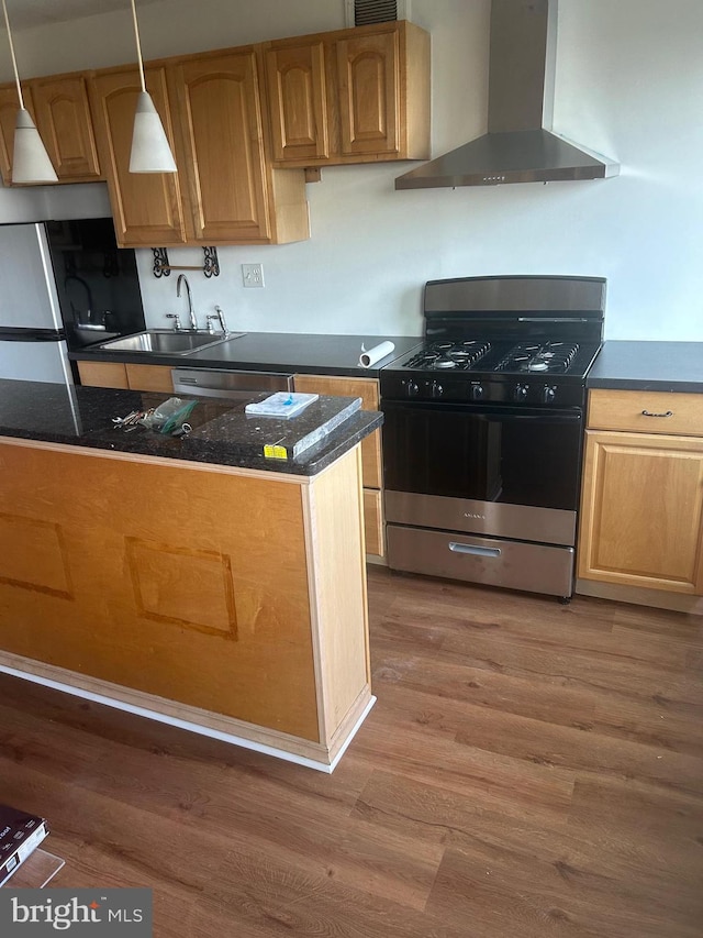 kitchen featuring wall chimney range hood, wood-type flooring, sink, pendant lighting, and appliances with stainless steel finishes