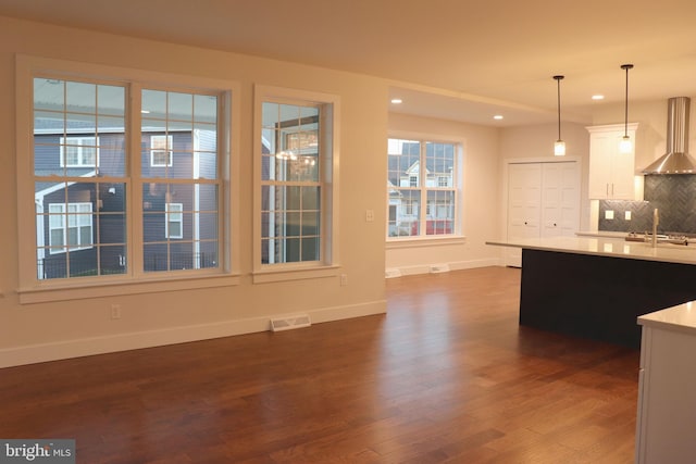 kitchen featuring wall chimney exhaust hood, white cabinetry, hanging light fixtures, and dark wood-type flooring