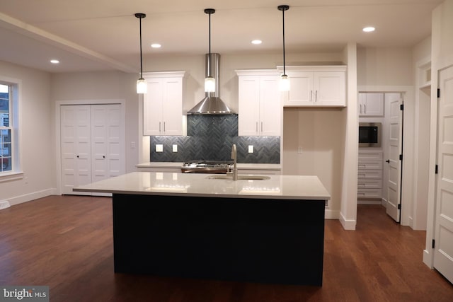 kitchen featuring wall chimney exhaust hood, white cabinetry, an island with sink, and dark wood-type flooring