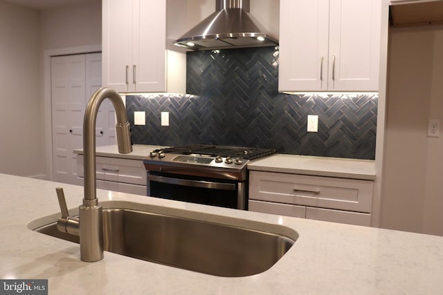 kitchen featuring wall chimney range hood, sink, stainless steel gas range, decorative backsplash, and white cabinetry