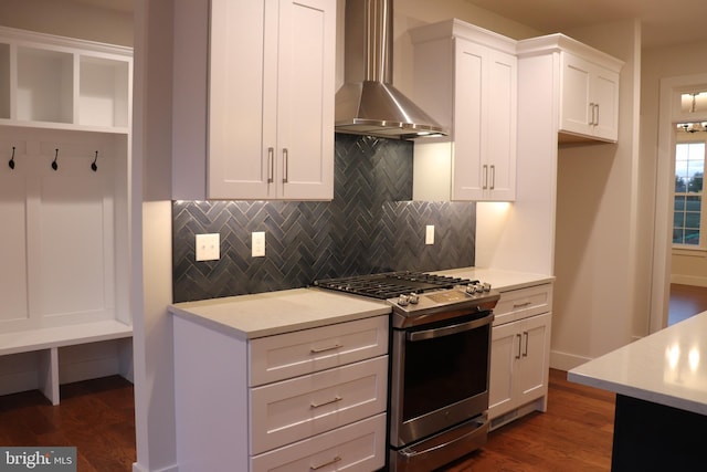 kitchen with dark wood-type flooring, wall chimney range hood, gas range, decorative backsplash, and white cabinetry