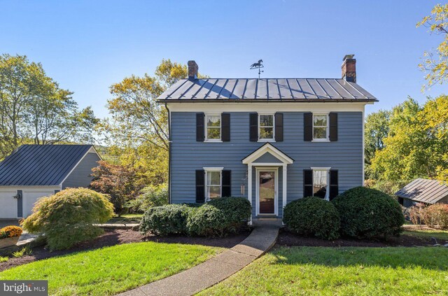 colonial inspired home featuring metal roof, a front lawn, a standing seam roof, and a chimney