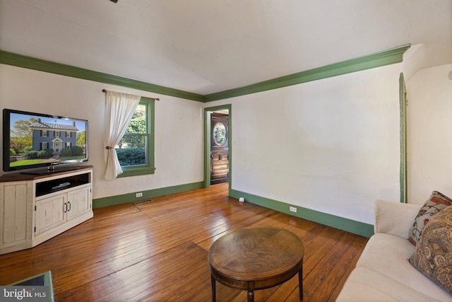living area with baseboards, hardwood / wood-style floors, visible vents, and crown molding
