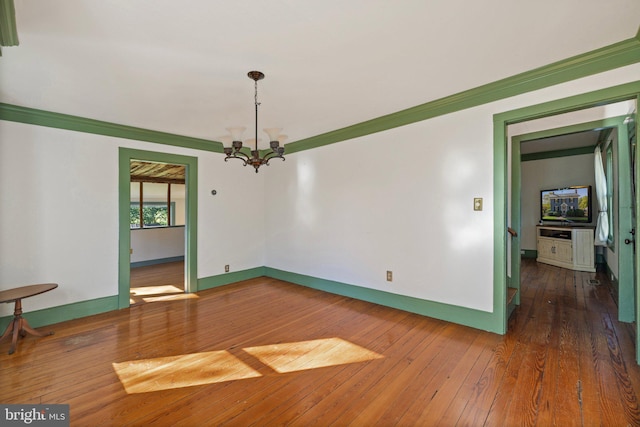 empty room featuring a chandelier, hardwood / wood-style flooring, crown molding, and baseboards