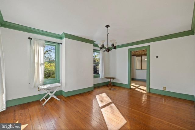 unfurnished dining area featuring an inviting chandelier, hardwood / wood-style flooring, baseboards, and ornamental molding