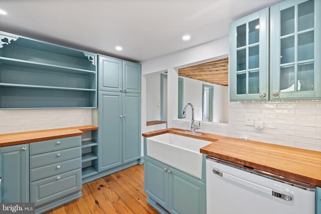 kitchen featuring a sink, tasteful backsplash, open shelves, white dishwasher, and wooden counters