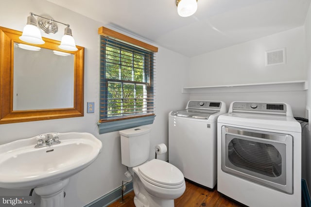 half bathroom featuring toilet, visible vents, a sink, wood finished floors, and washing machine and clothes dryer