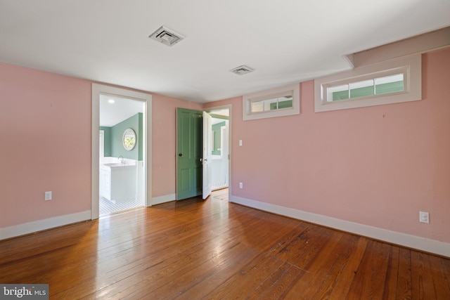 empty room with hardwood / wood-style flooring, baseboards, and visible vents