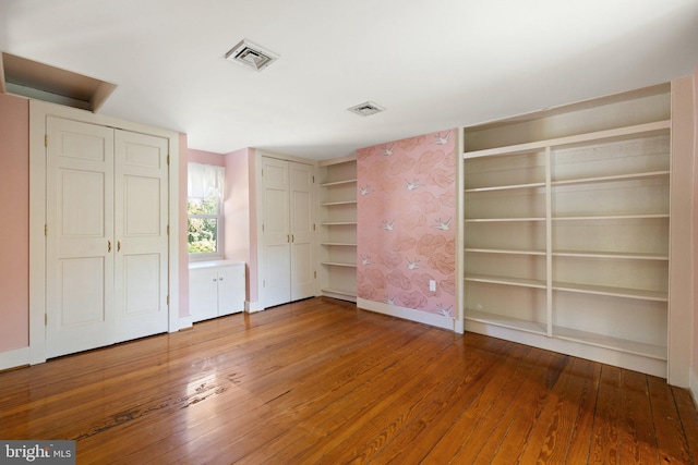 unfurnished bedroom featuring two closets, wood-type flooring, baseboards, and visible vents