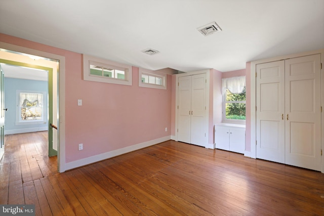 unfurnished bedroom featuring multiple closets, visible vents, baseboards, and hardwood / wood-style floors