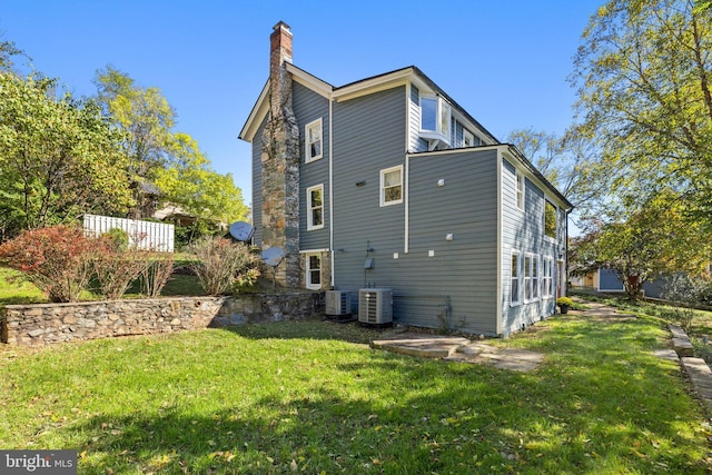 back of property featuring a chimney, cooling unit, and a lawn